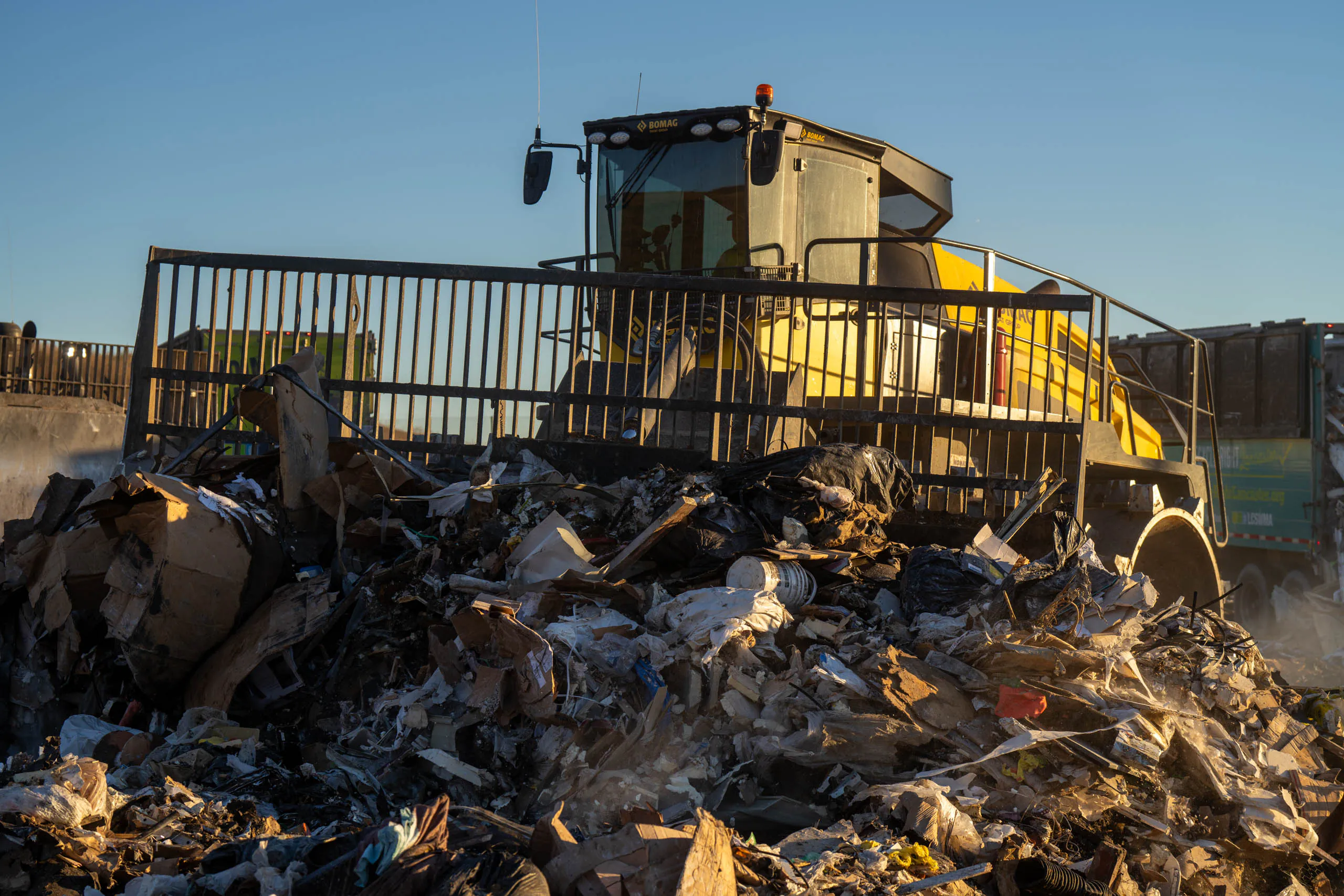 A yellow landfill compactor pushes a large pile of mixed garbage and debris at Frey Farm Landfill, demonstrating efficient waste management under a clear blue sky.
