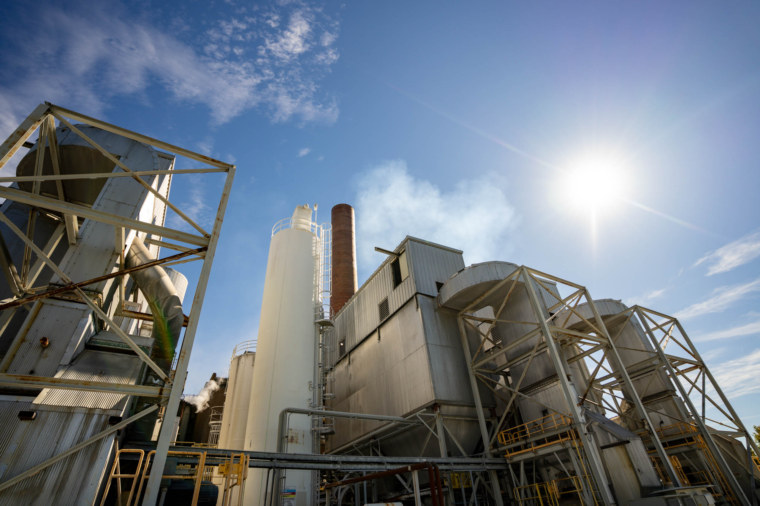 lcswma industrial facility with silos, metal structures, and chimneys emits steam under a bright sunny sky, highlighting its commitment to sustainable energy and clean energy solutions as the sun shines in the upper right corner.