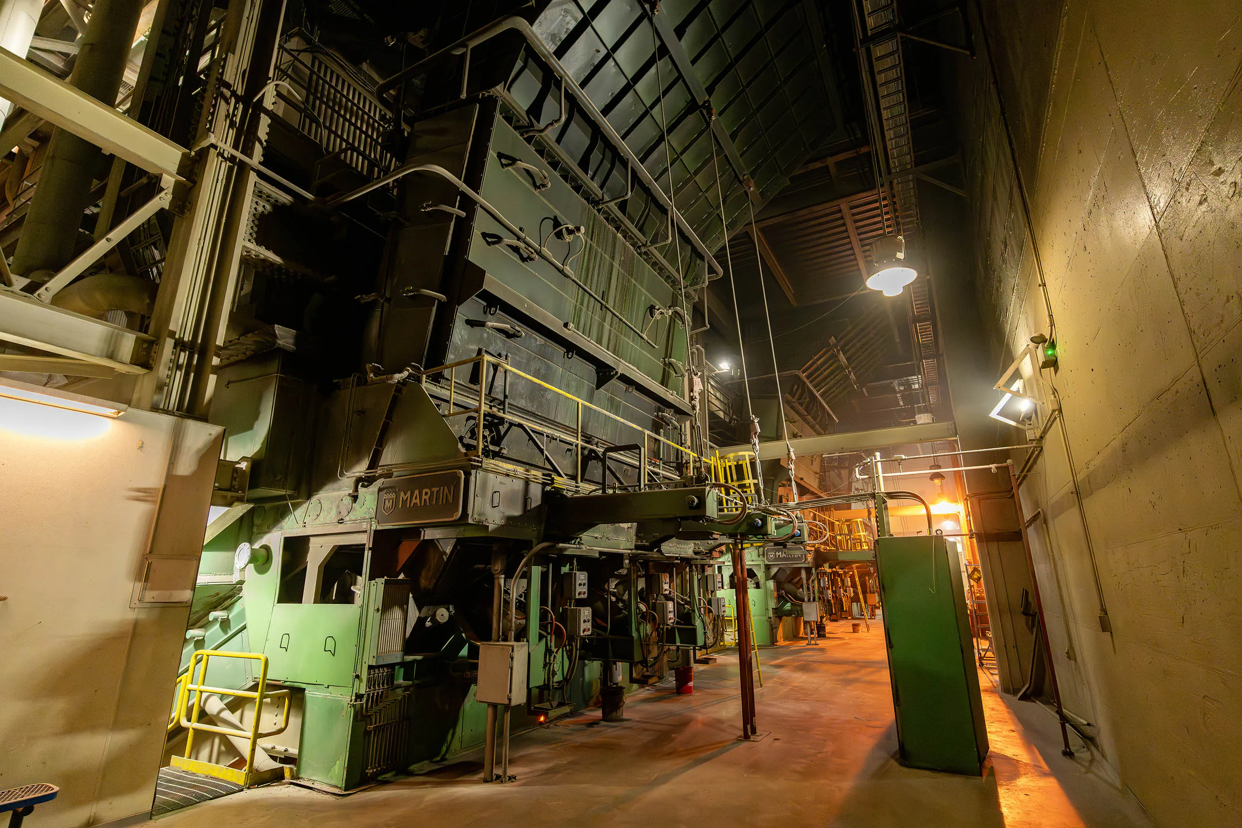 A large, industrial paper machine with metal walkways and pipes inside a factory, illuminated by overhead lights, highlights the Rethinking Waste approach to modern manufacturing.