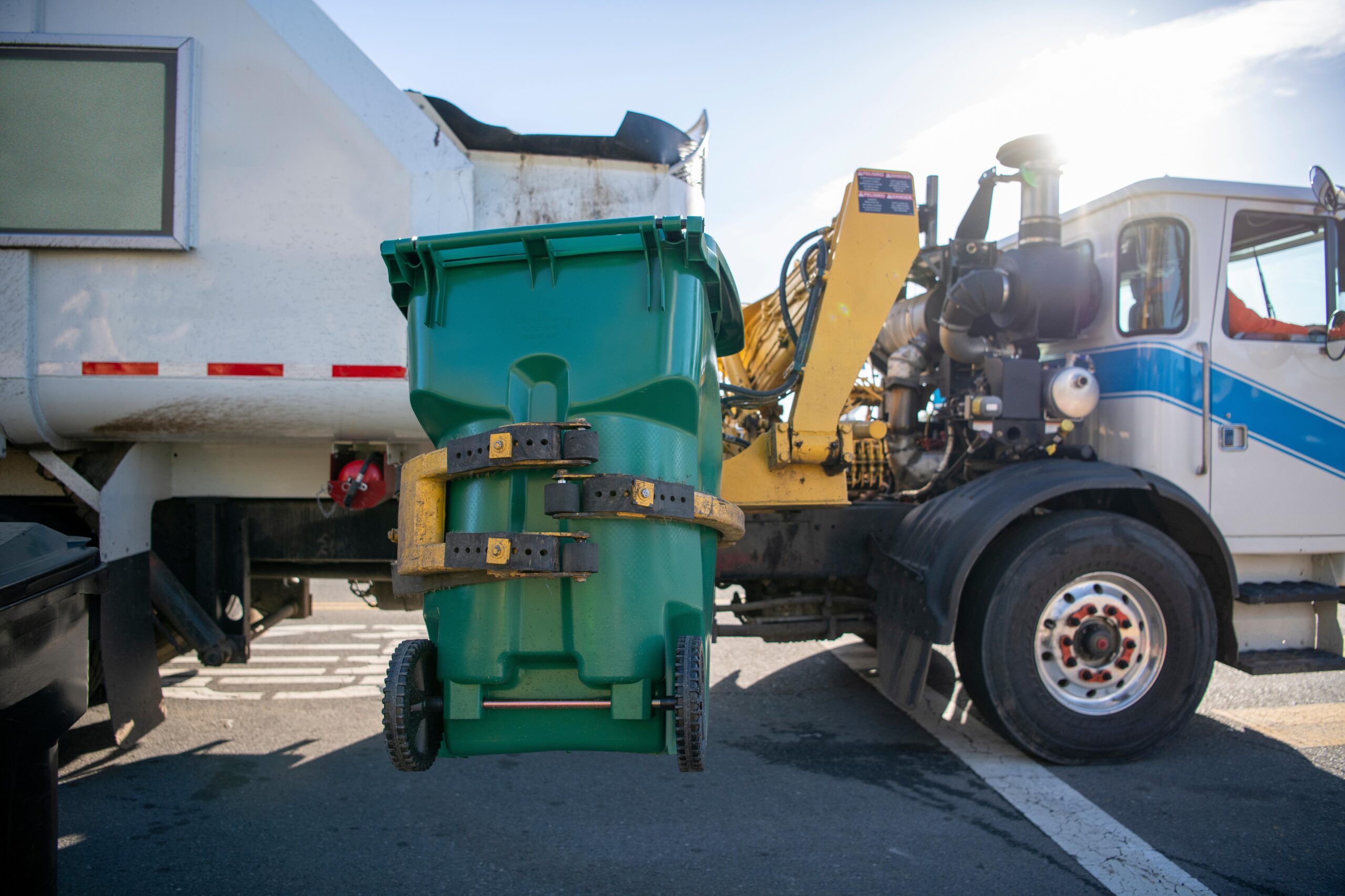 Residential green trash bin being lifted to dump waste in truck