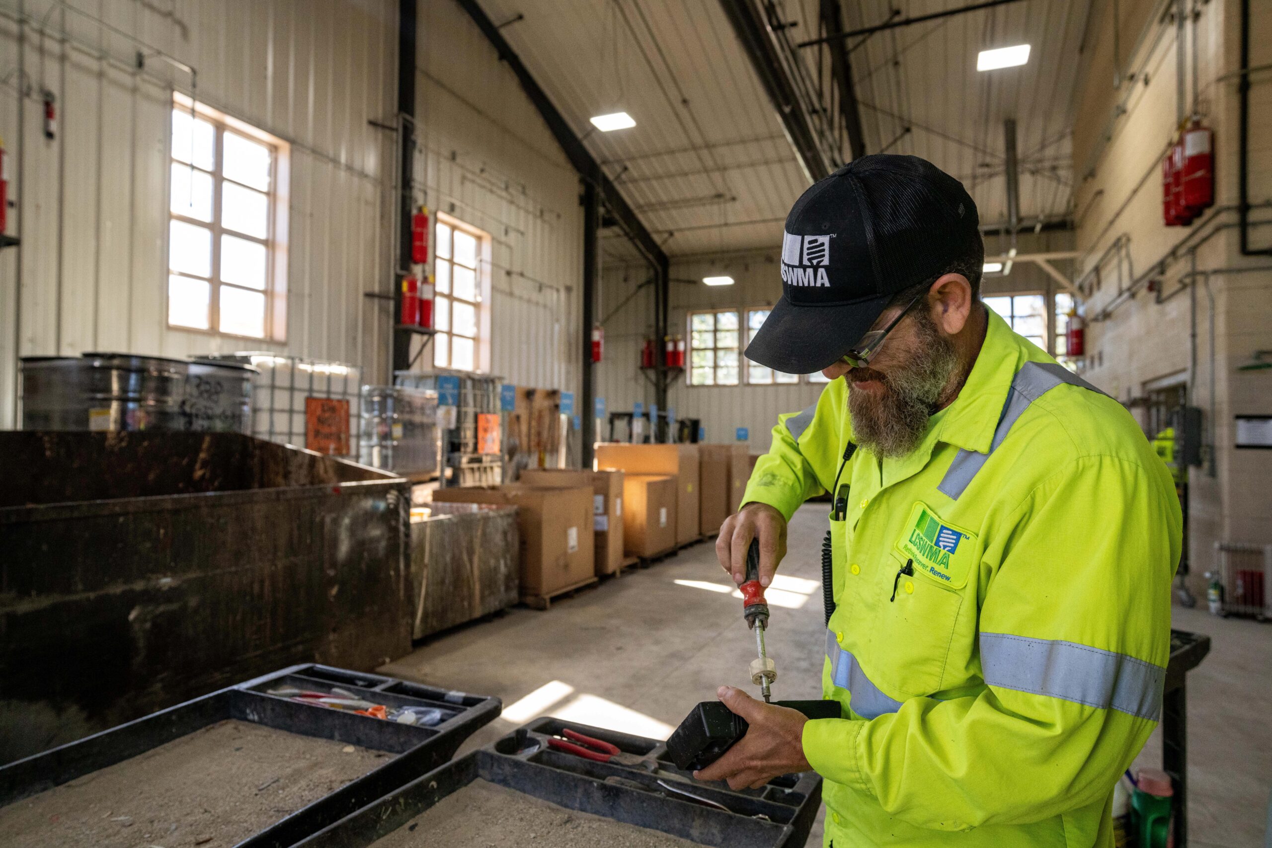 Close up side profile of worker wearing neon yellow clothing in a room full of supplies. Using screwdriver on object in hand.